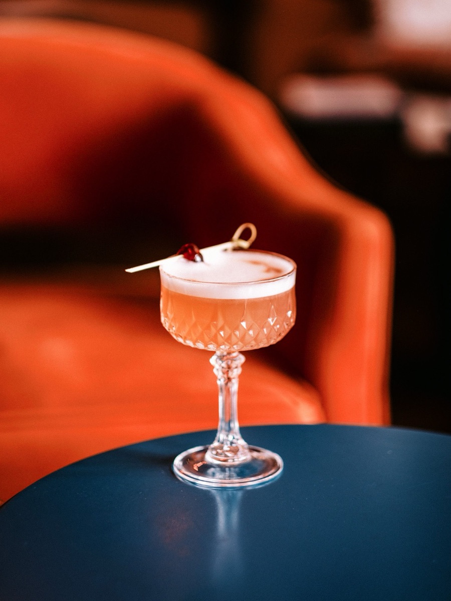 A signature cocktail on a blue table against a velvet orange chair at Fiona's Bartique
